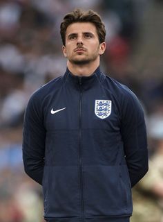 a man standing on top of a soccer field wearing a blue and white jacket with the england crest on it