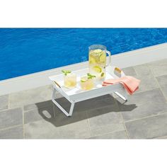 an outdoor table with drinks on it next to a swimming pool and blue water in the background