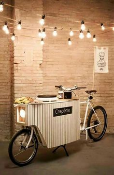 a bike is parked next to a small ice cream cart with lights on the wall