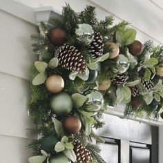 a christmas wreath with pine cones and greenery hanging from the side of a door