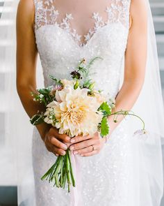 a woman in a wedding dress holding a bouquet of white and yellow flowers with greenery