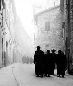 three men are walking down the street in an old town with stone buildings and cobblestone streets