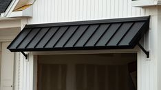 a black awning on the side of a white house next to a cat sitting in an open window