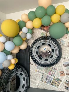 some balloons are hanging from the ceiling next to a tire and car wheel on top of newspaper pages