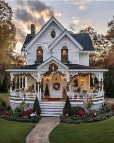 a white house decorated for christmas with wreaths on the front porch and stairs leading up to it