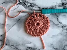 the crochet hook is laying on top of the marble counter next to an orange yarn ball