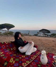 a woman sitting on top of a red blanket next to a white vase and potted plant