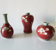 three red vases sitting on top of a white table next to each other with flowers painted on them