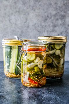 three jars filled with pickles and other vegetables on top of a black countertop