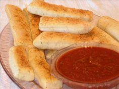 some bread sticks are on a plate with ketchup in a bowl next to them