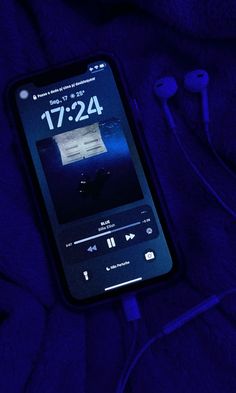 an iphone with ear buds and headphones laying on a purple blanket in the dark