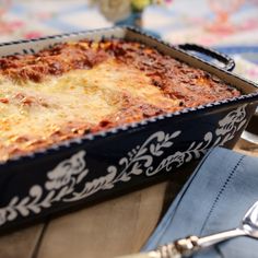 a casserole dish with meat and cheese in it on a table next to two silver spoons