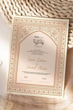 an ornate wedding card with gold foil on it, sitting next to a woven basket