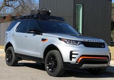 a white land rover is parked in front of a building with black rims and an aluminum roof rack