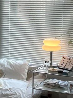 a lamp sitting on top of a glass table next to a window with white blinds