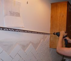 a woman is using a drill to paint the wall in her kitchen with white tile