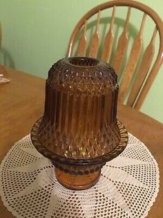 a brown glass candle holder sitting on top of a wooden dining room table with white doily