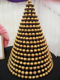 a chocolate christmas tree made out of gold foil wrapped cookies and candy balls on a black table