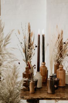 a table topped with vases filled with plants and candles next to each other on top of a wooden table