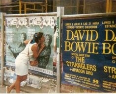 a woman leaning against a poster on the side of a building in front of another sign