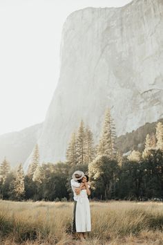 a man and woman standing in front of a large mountain with trees on the other side