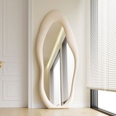 a mirror sitting on top of a wooden floor next to a window covered in blinds