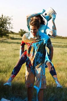 a man with paint all over his body and head walking through the grass carrying a bucket on his shoulders