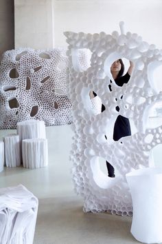 a woman standing in front of a sculpture made out of white paper and plastic cups