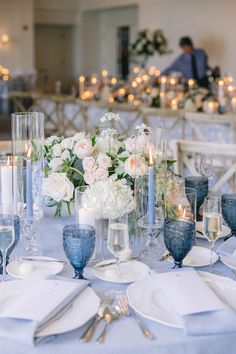 the table is set with white flowers and blue vases, silverware and candles