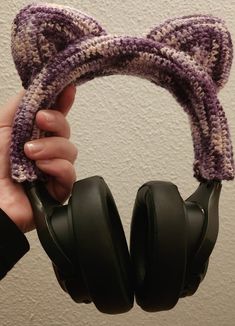 a person holding up some headphones in front of a wall with a cat ears on it