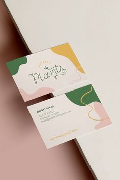 two business cards sitting on top of each other next to a white table with pink and green designs