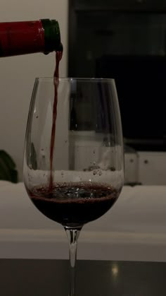 a wine glass filled with red wine being poured into it