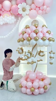 a man kneeling down next to a bunch of pink and white balloons in the shape of a tree