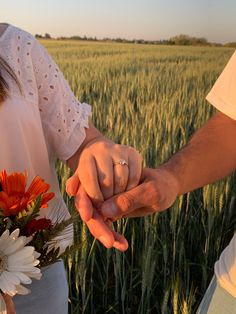 two people holding hands while standing in front of a wheat field with sunflowers