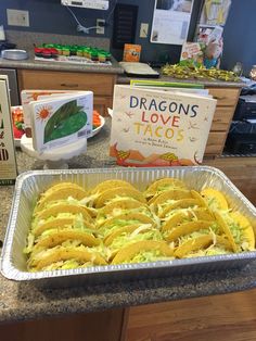 a pan filled with tacos sitting on top of a counter next to a book