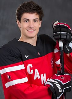 a young man in red and black jersey holding a hockey stick with both hands on his shoulder