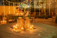 two vases filled with flowers and lit candles on top of a table covered in lights