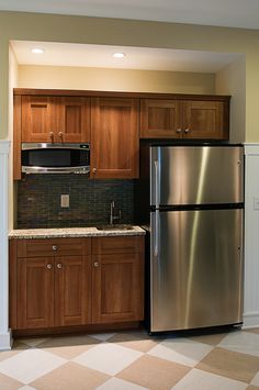 a stainless steel refrigerator in a kitchen next to wooden cabinets and checkered flooring