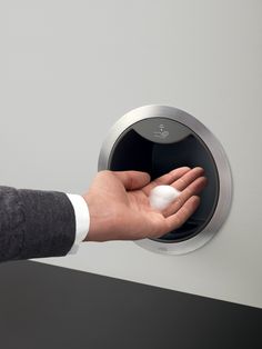 a person's hand is pressing the button on a wall mounted toilet paper dispenser