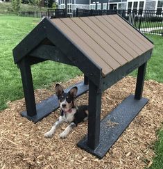 a small dog laying under a wooden structure on top of some hay in the yard