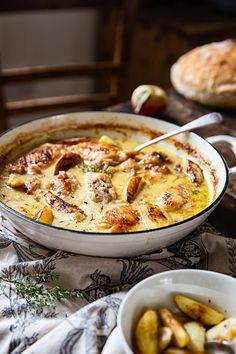 a casserole dish with potatoes and meat in it on a table next to bread