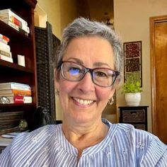 an older woman wearing glasses sitting in front of a book shelf with books on it