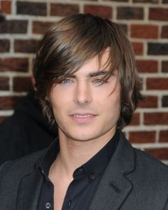 a close up of a person wearing a suit and tie with a brick wall in the background