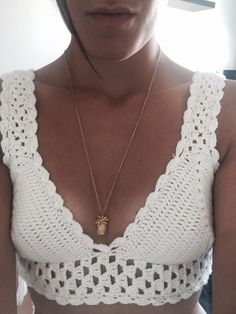 a woman wearing a white crochet top with a pineapple pendant on it