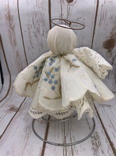 a white cloth doll with blue flowers on it sitting on a metal stand in front of a wooden wall