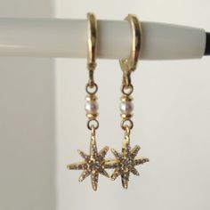 These Dainty North Star Earrings, featuring a starburst design, are perfect for any occasion. Easy to wear and striking in appearance, these earrings are an ideal gift for birthdays, anniversaries, bridesmaids, friends, sisters, and as a Christmas present. The combination of cubic zirconia and Swarovski pearls adds a touch of glamour, making these earrings a delightful addition to any jewelry collection. Details: Earring Hooks: Huggie Hoop. Material: 14k thick gold plated over brass. Stones: Cub Celestial Star-shaped Sparkling Earrings, Sparkling Star-shaped Celestial Earrings, Gold Star-shaped Crystal Earrings For Pierced Ears, Earrings Starburst, Gold Star Earrings, Starburst Design, Earrings Dangling, Starburst Earrings, Simple Gifts