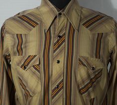 We LOVE this 70's Wrangler's western shirt! This made in USA and quite collectible ranch shirt has a cool, lightweight striped material, pearly snaps, diamond pockets and back yoke. You'll treasure this more rare find. This vintage Wrangler's cowboy long tail, long sleeve tailored top makes a wonderful addition to your collection of western shirts. This western shirt is in decent pre-loved condition with signs of wear/fade/use/loose threads. The vintage 70s Wrangler's brand label says it is made Vintage Shirt For Western-themed Fall Events, Vintage Cotton Shirt For Rodeo, Retro Western Shirt For Fall, Vintage Collared Shirt For Rodeo, Retro Long Sleeve Shirt For Ranch, Vintage Collared Tops For Rodeo, Vintage Brown Tops For Ranch, Retro Collared Tops For Rodeo, Vintage Long Sleeve Shirt For Western-themed Events