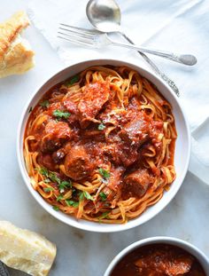 a bowl of spaghetti with meatballs and tomato sauce next to bread on a table