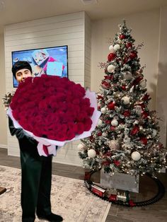 a man holding a large bouquet of roses in front of a christmas tree