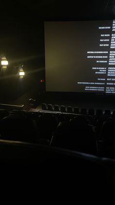 an auditorium with rows of seats in front of a projector screen and lights on the wall